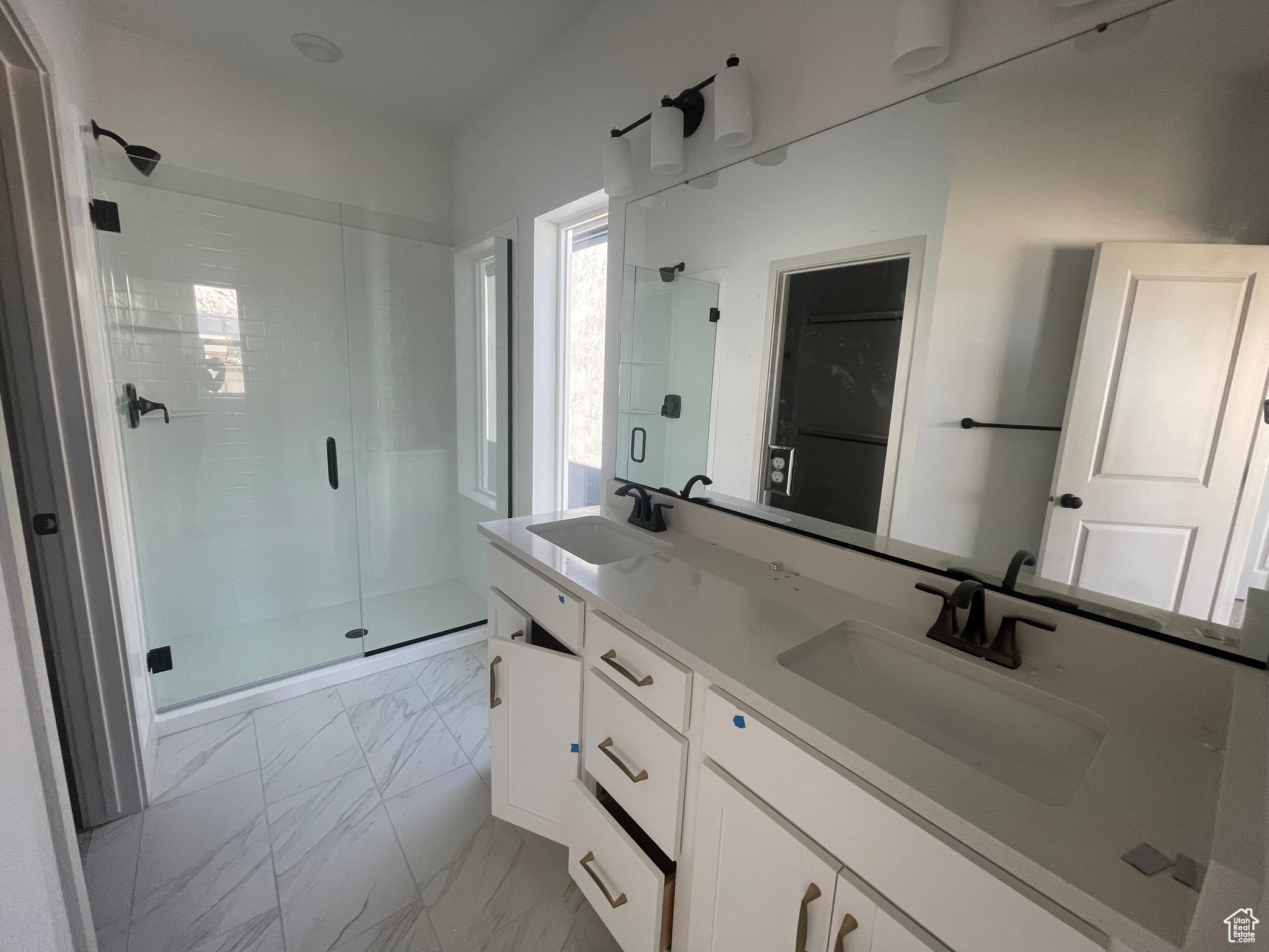 Bathroom with a shower with shower door, tile floors, and double vanity