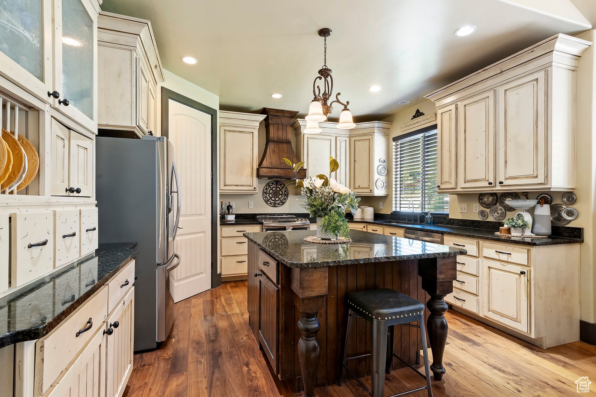 Kitchen featuring a kitchen island, premium range hood, wood-type flooring, dark stone countertops, and stainless steel appliances