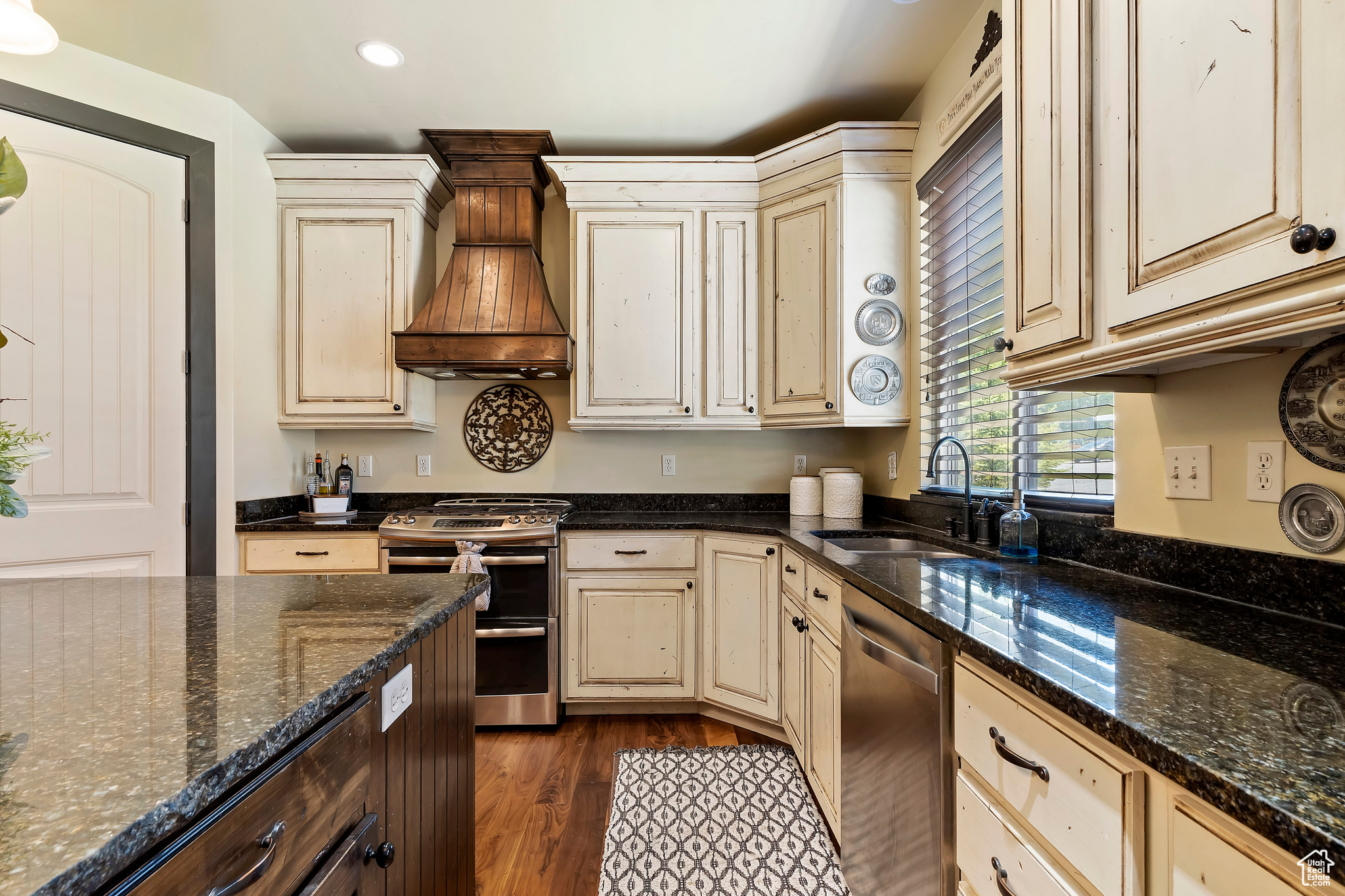 Kitchen with custom range hood, appliances with stainless steel finishes, dark stone counters, and sink