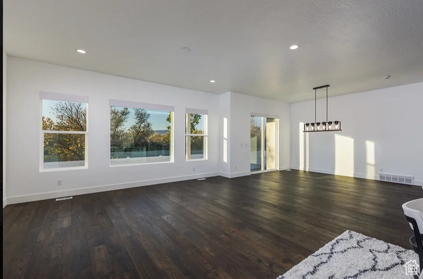 Unfurnished living room featuring dark hardwood / wood-style flooring and a notable chandelier