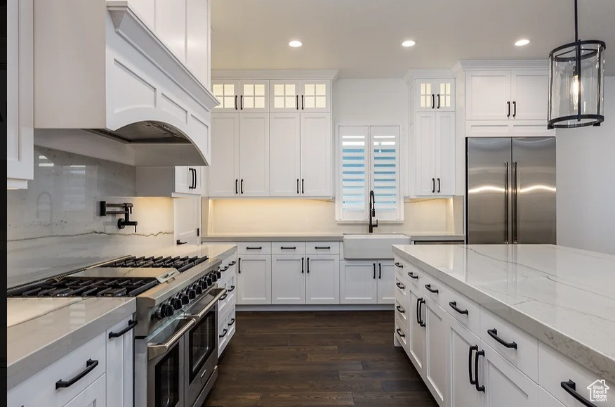 Kitchen with premium appliances, hanging light fixtures, white cabinets, sink, and dark wood-type flooring