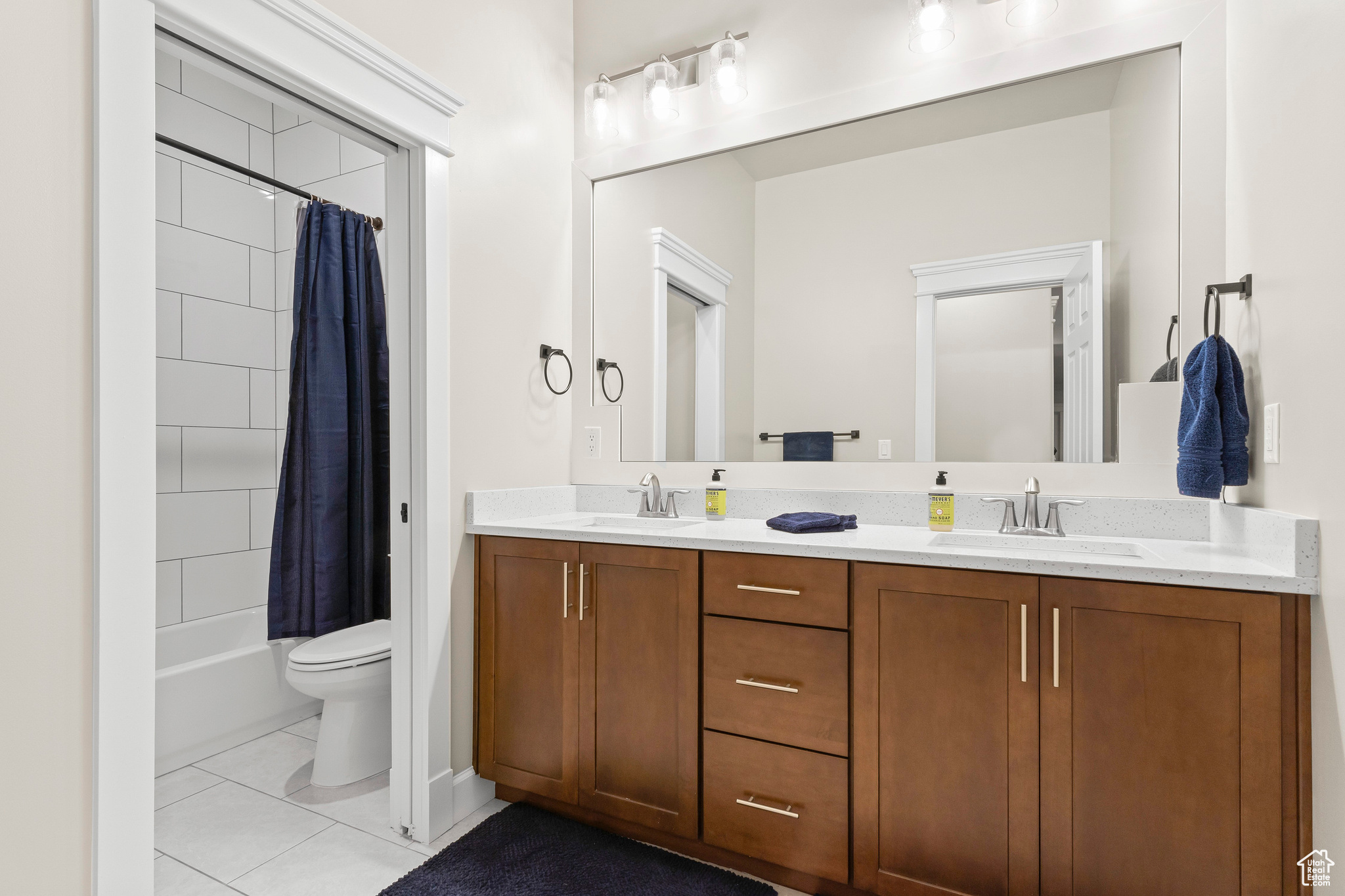 Full bathroom with double sink vanity, toilet, tile flooring, and shower / bathtub combination with curtain