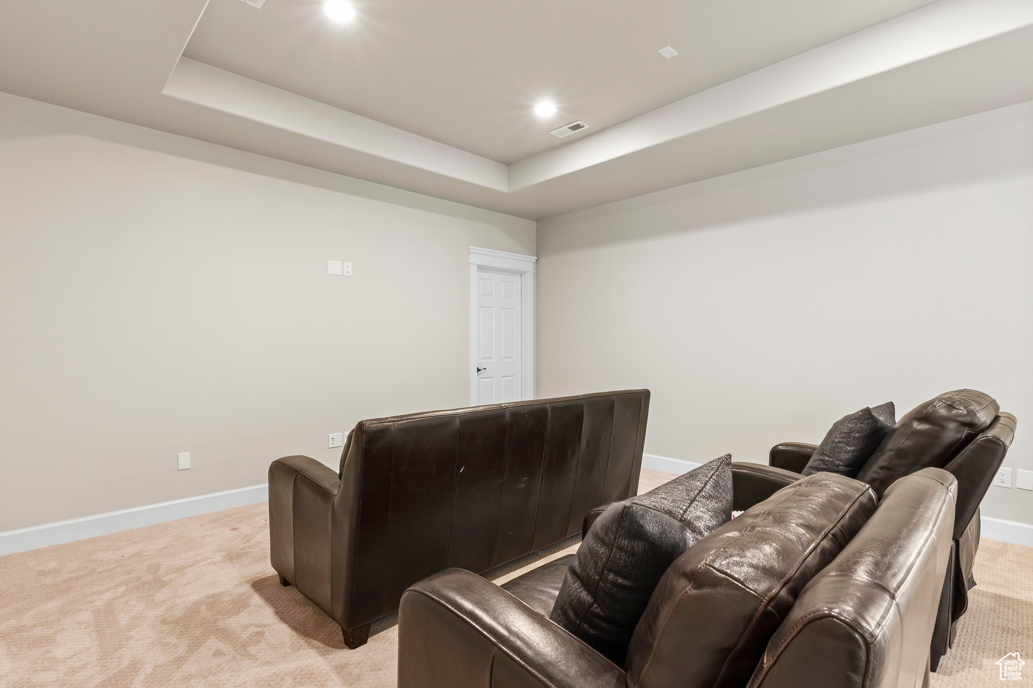 Home theater room with a raised ceiling and light carpet