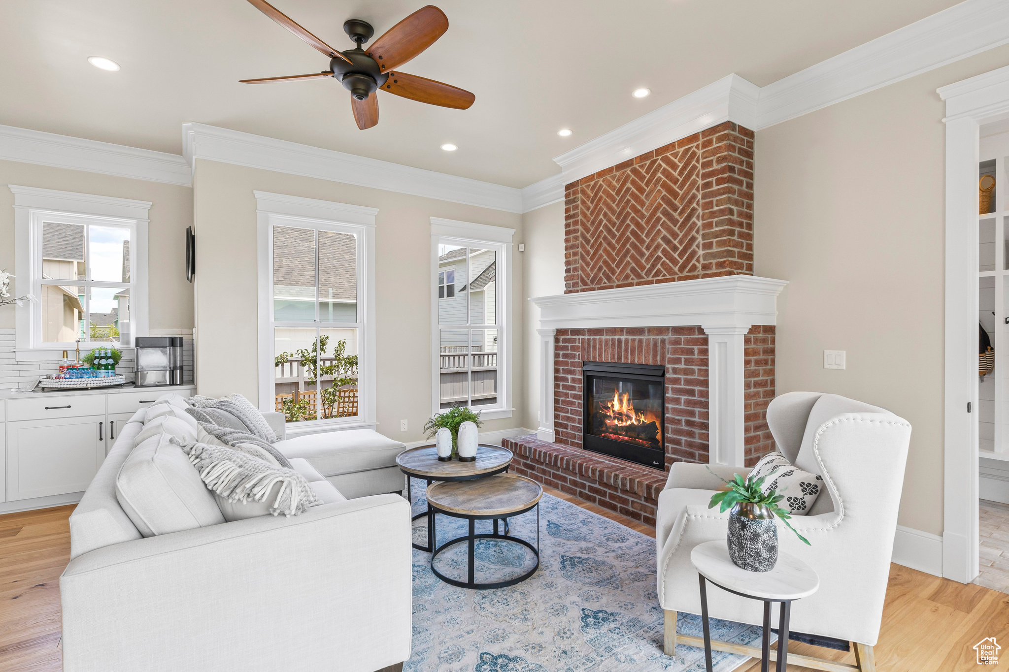 Living room with crown molding, light wood-type flooring, a brick fireplace, and ceiling fan