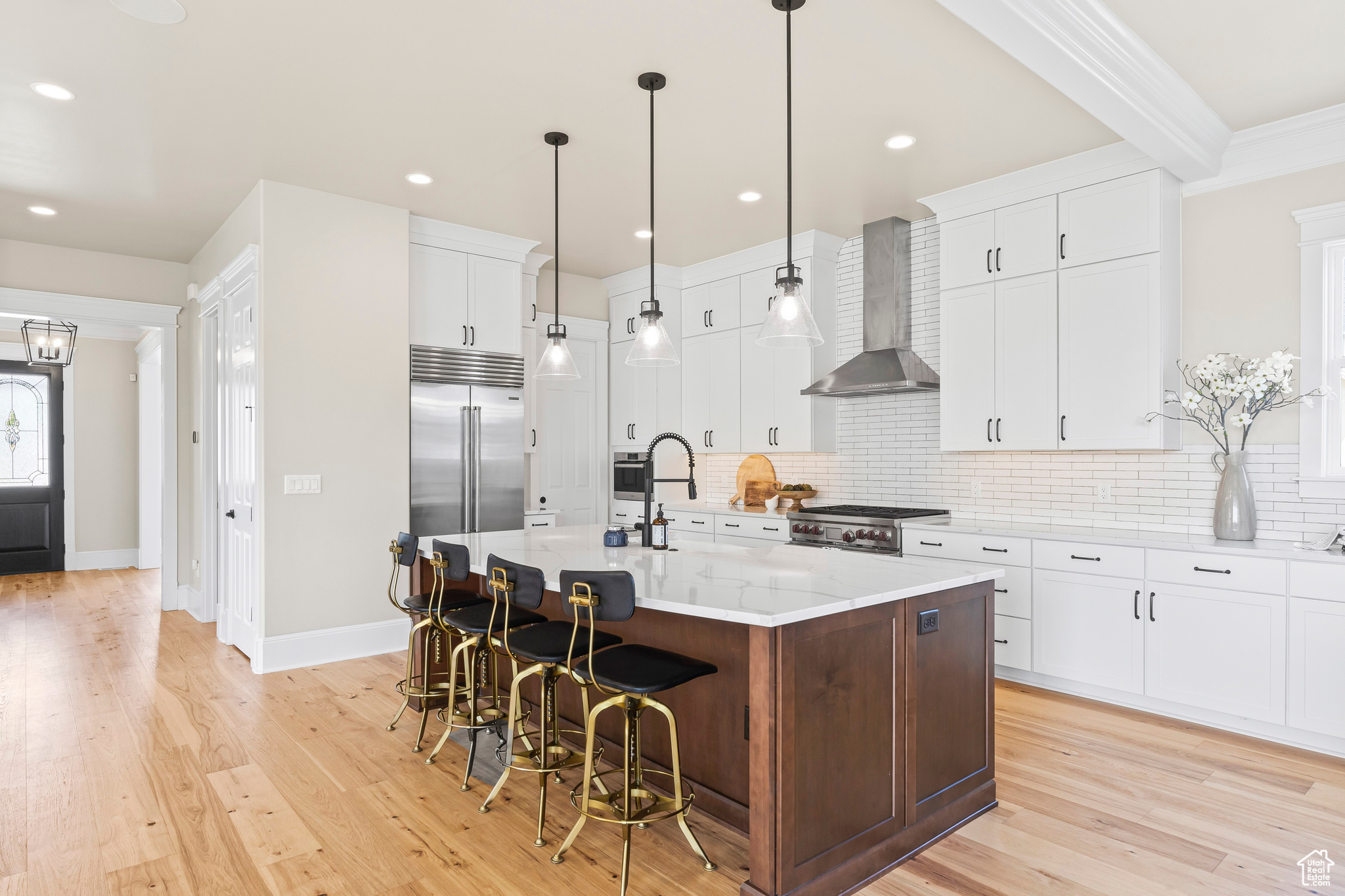 Kitchen featuring stove, wall chimney exhaust hood, light hardwood / wood-style flooring, a kitchen island with sink, and white cabinetry