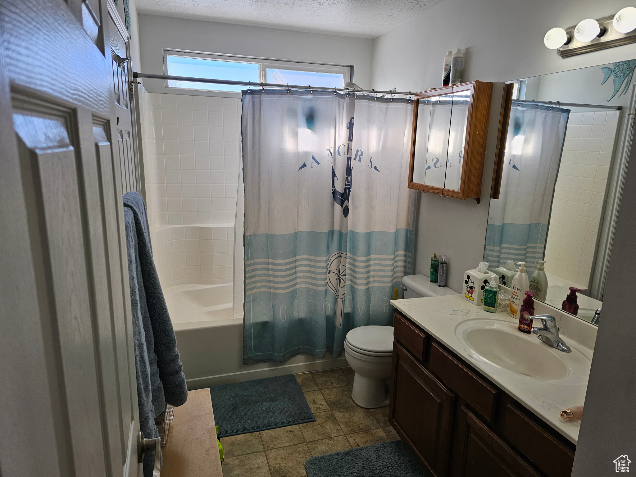 Full bathroom featuring a textured ceiling, large vanity, toilet, tile flooring, and shower / tub combo