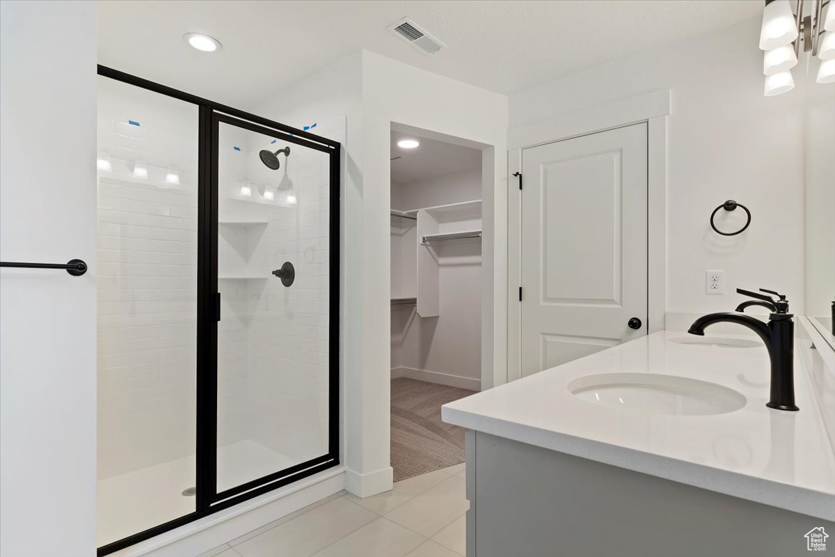 Bathroom with dual bowl vanity, tile flooring, and a shower with door