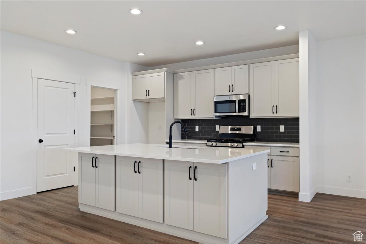 Kitchen featuring white cabinets, appliances with stainless steel finishes, an island with sink, and dark hardwood / wood-style floors