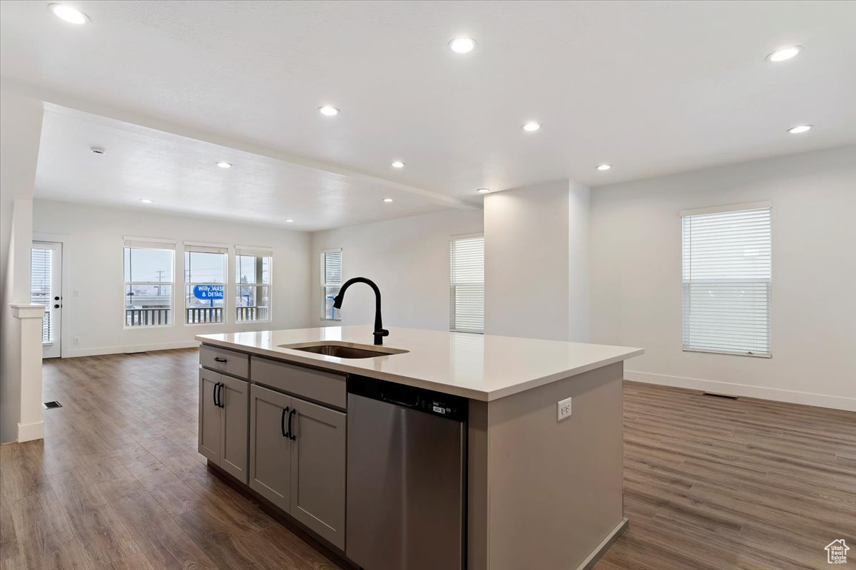 Kitchen featuring sink, dark wood-type flooring, a center island with sink, dishwasher, and gray cabinetry