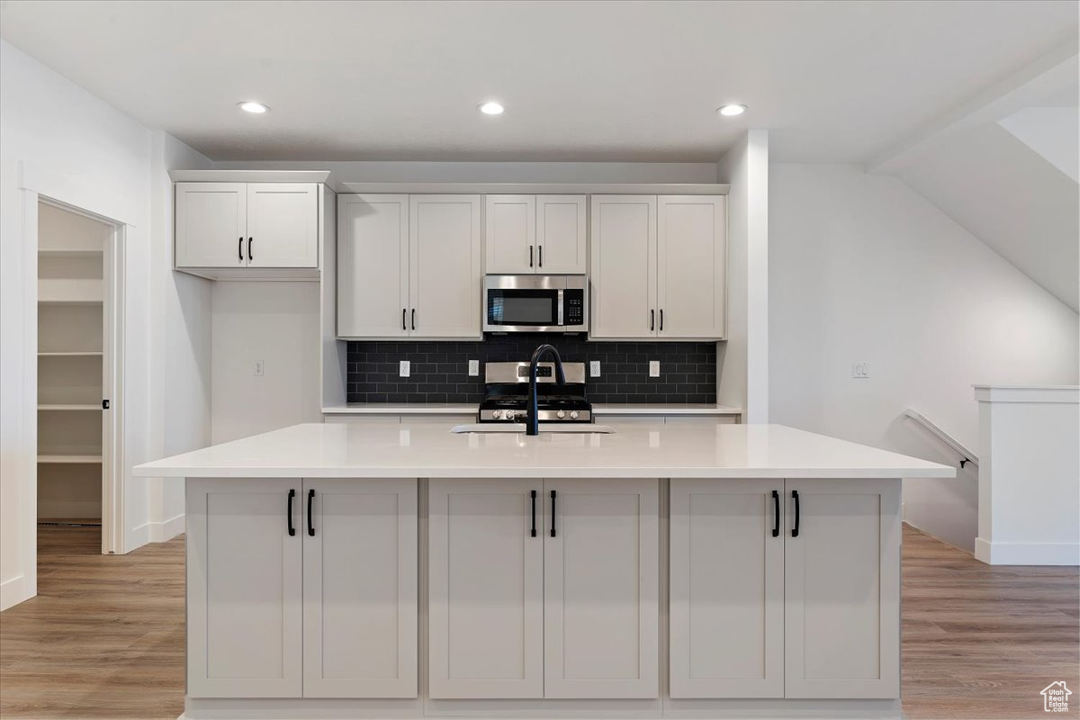 Kitchen with a kitchen island with sink, white cabinetry, and light wood-type flooring