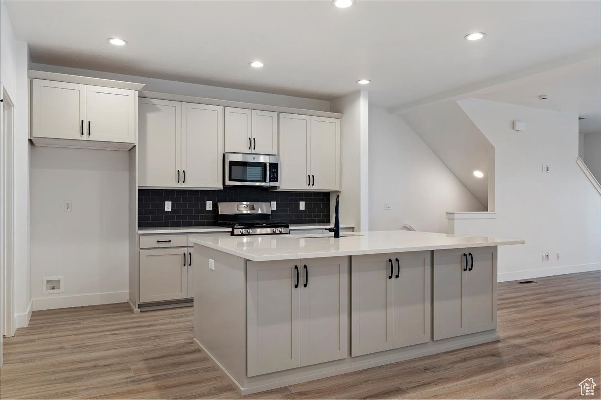 Kitchen with white cabinets, light hardwood / wood-style floors, a kitchen island with sink, and stove