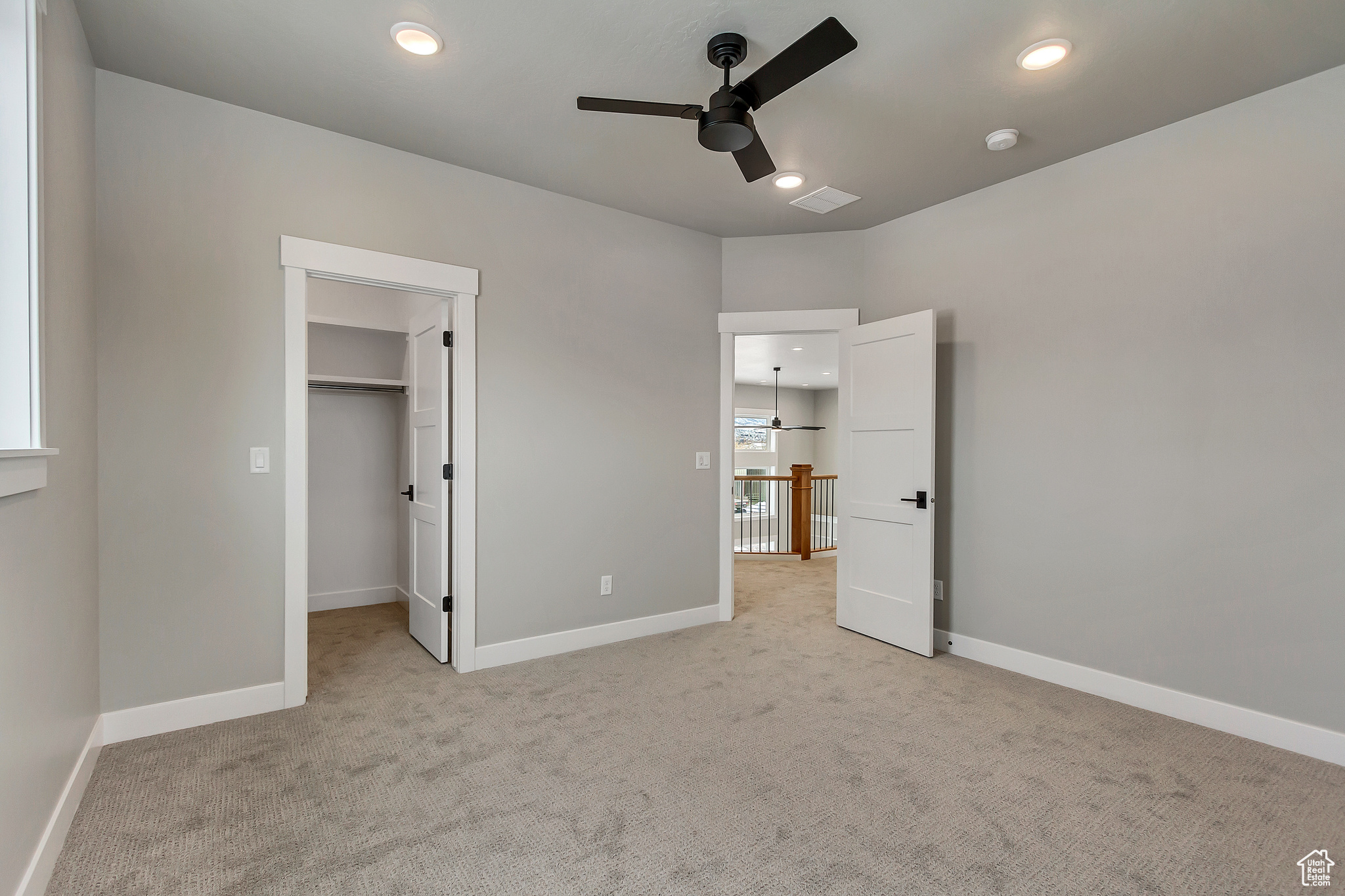 Unfurnished bedroom featuring light carpet, a closet, a spacious closet, and ceiling fan