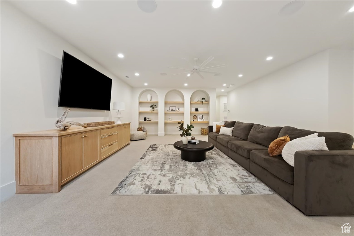 Carpeted living room with built in shelves and ceiling fan
