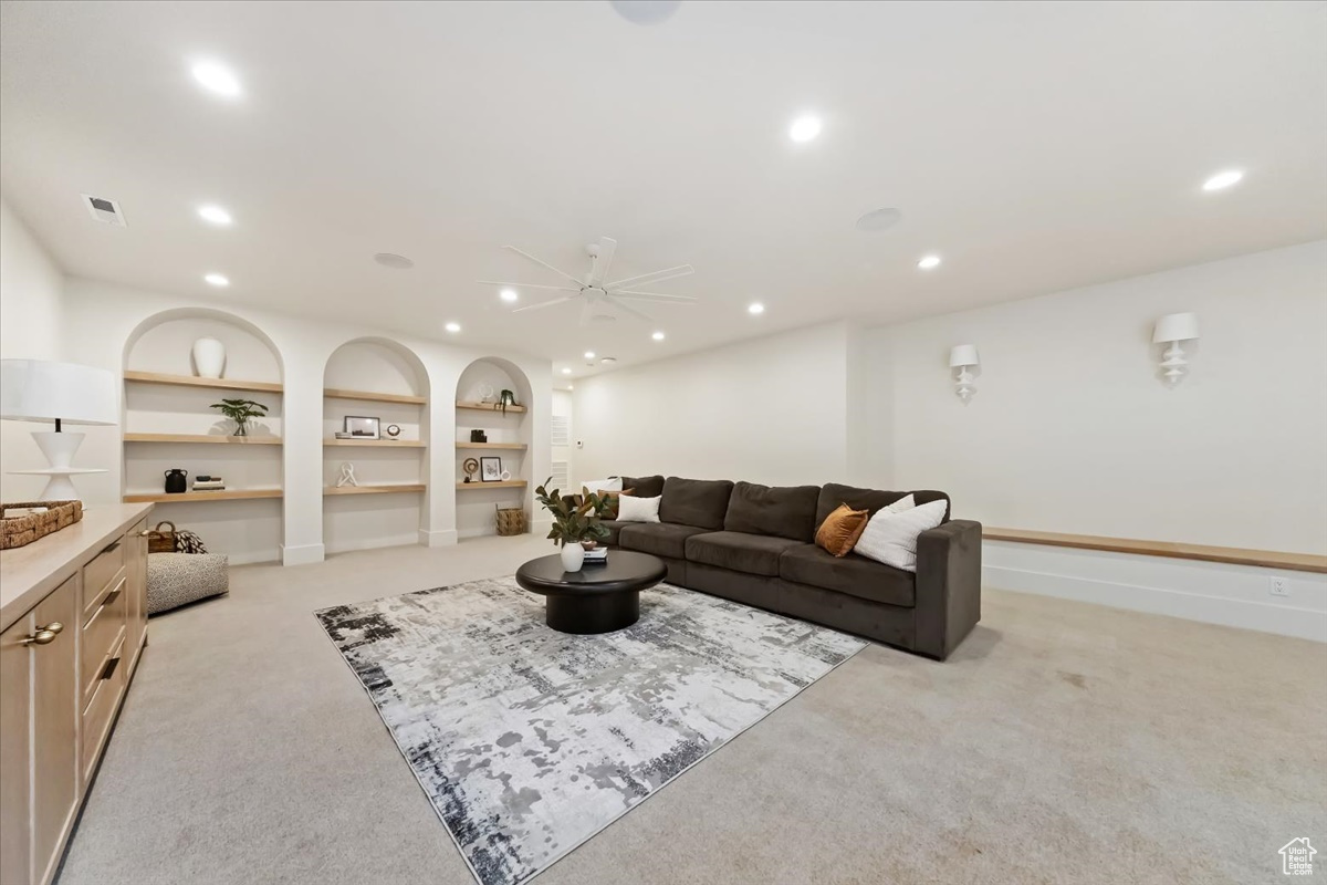Carpeted living room featuring built in shelves and ceiling fan