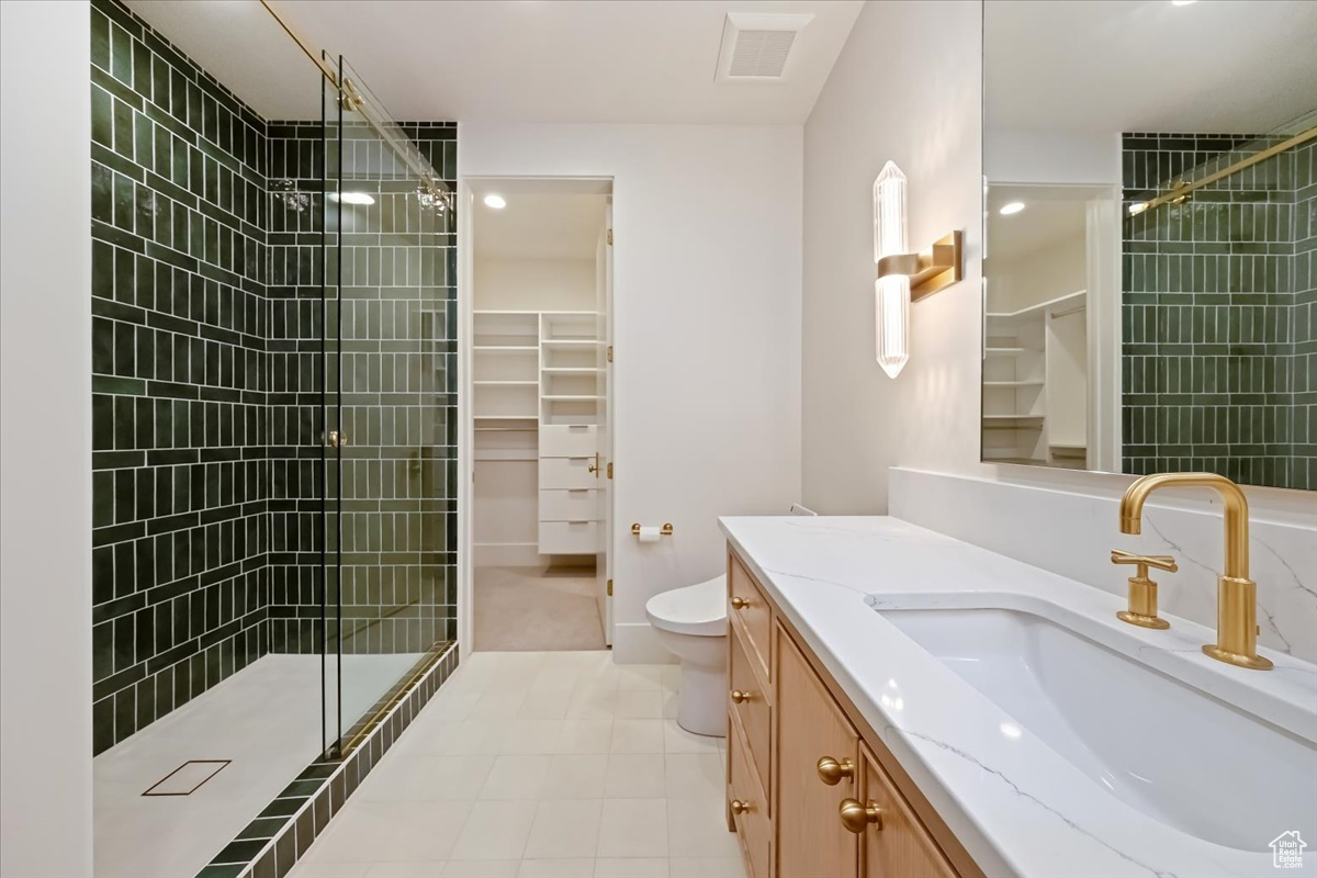 Bathroom featuring a shower with shower door, tile floors, toilet, and oversized vanity
