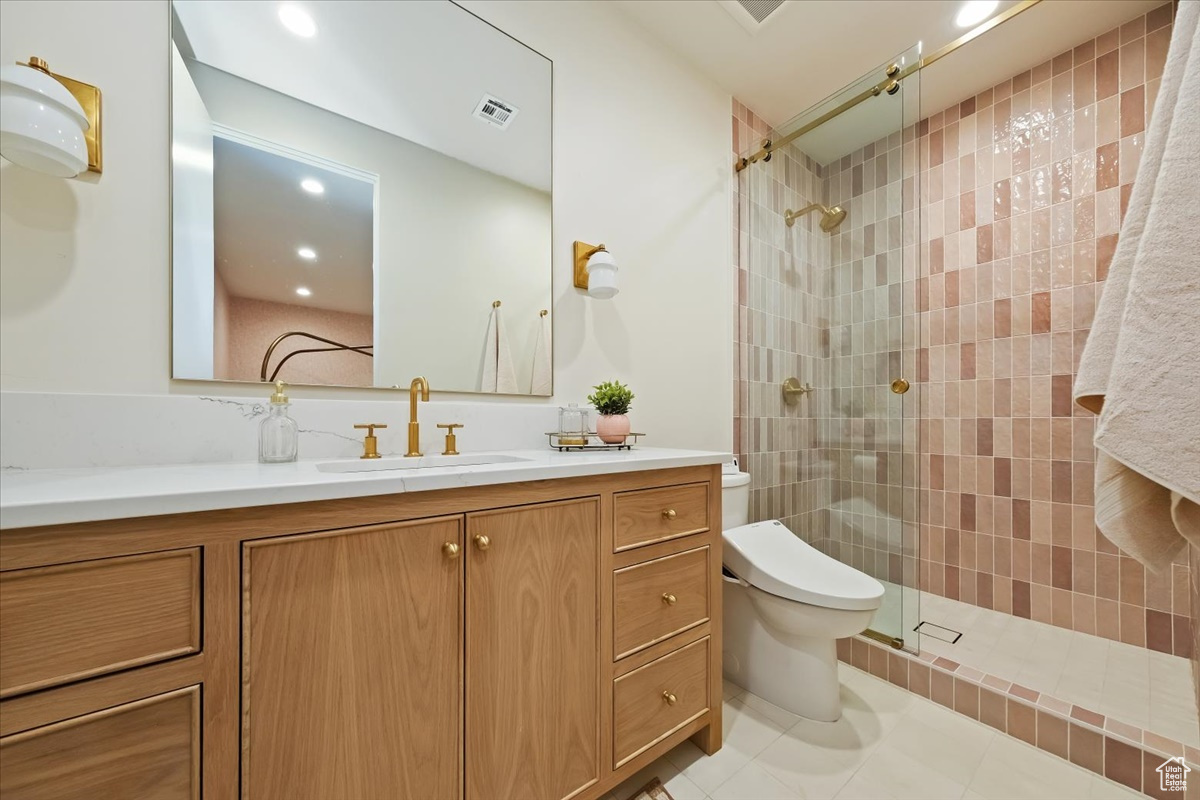 Bathroom featuring tile flooring, vanity, toilet, and tiled shower