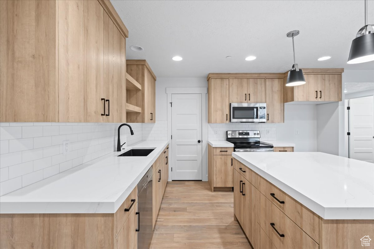 Kitchen featuring pendant lighting, backsplash, light hardwood / wood-style flooring, sink, and stainless steel appliances