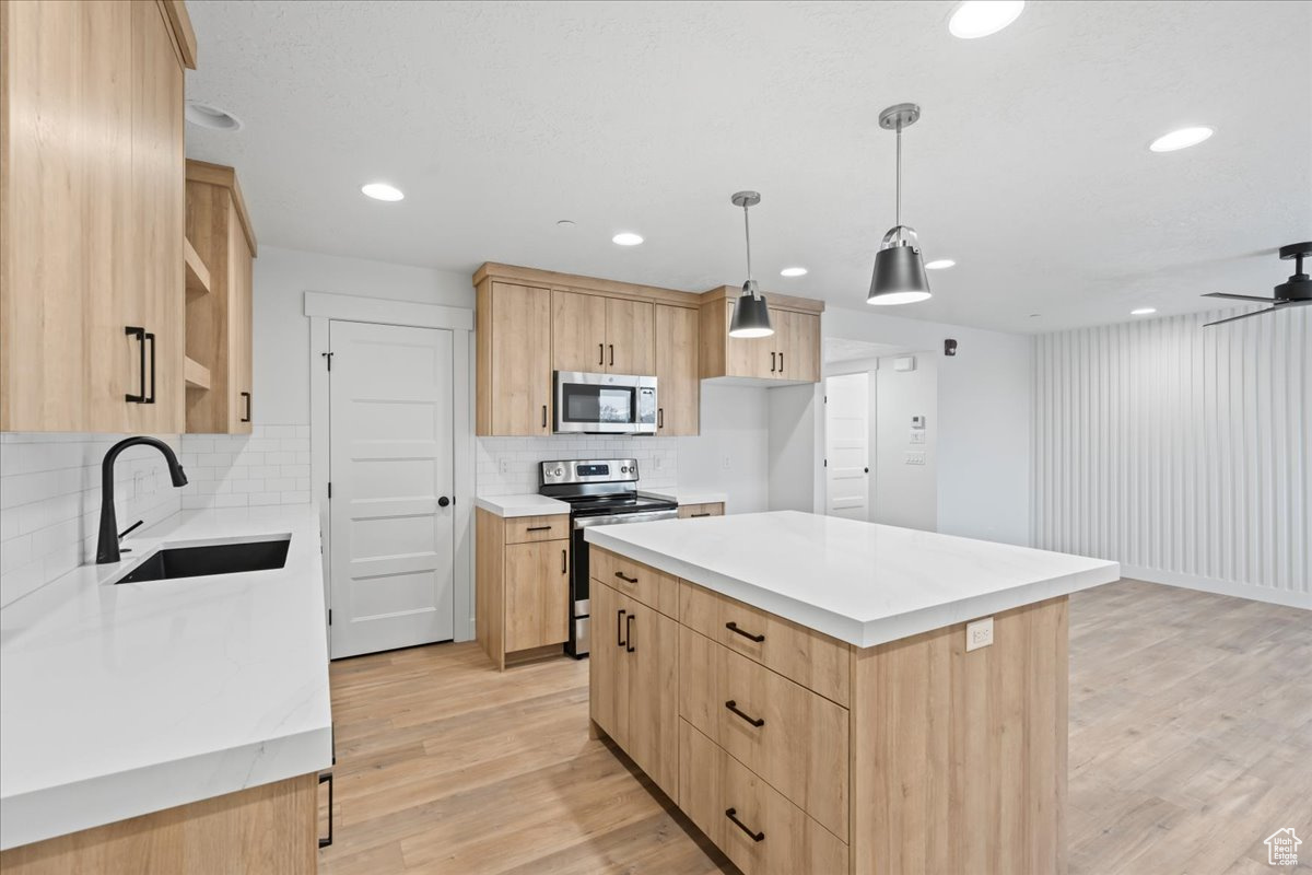 Kitchen featuring stainless steel appliances, light wood-type flooring, a kitchen island, ceiling fan, and tasteful backsplash