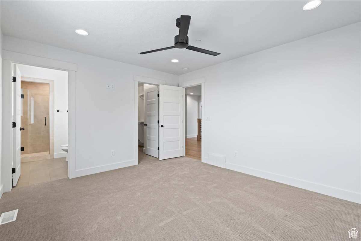 Unfurnished bedroom featuring light carpet, a walk in closet, ensuite bath, and ceiling fan