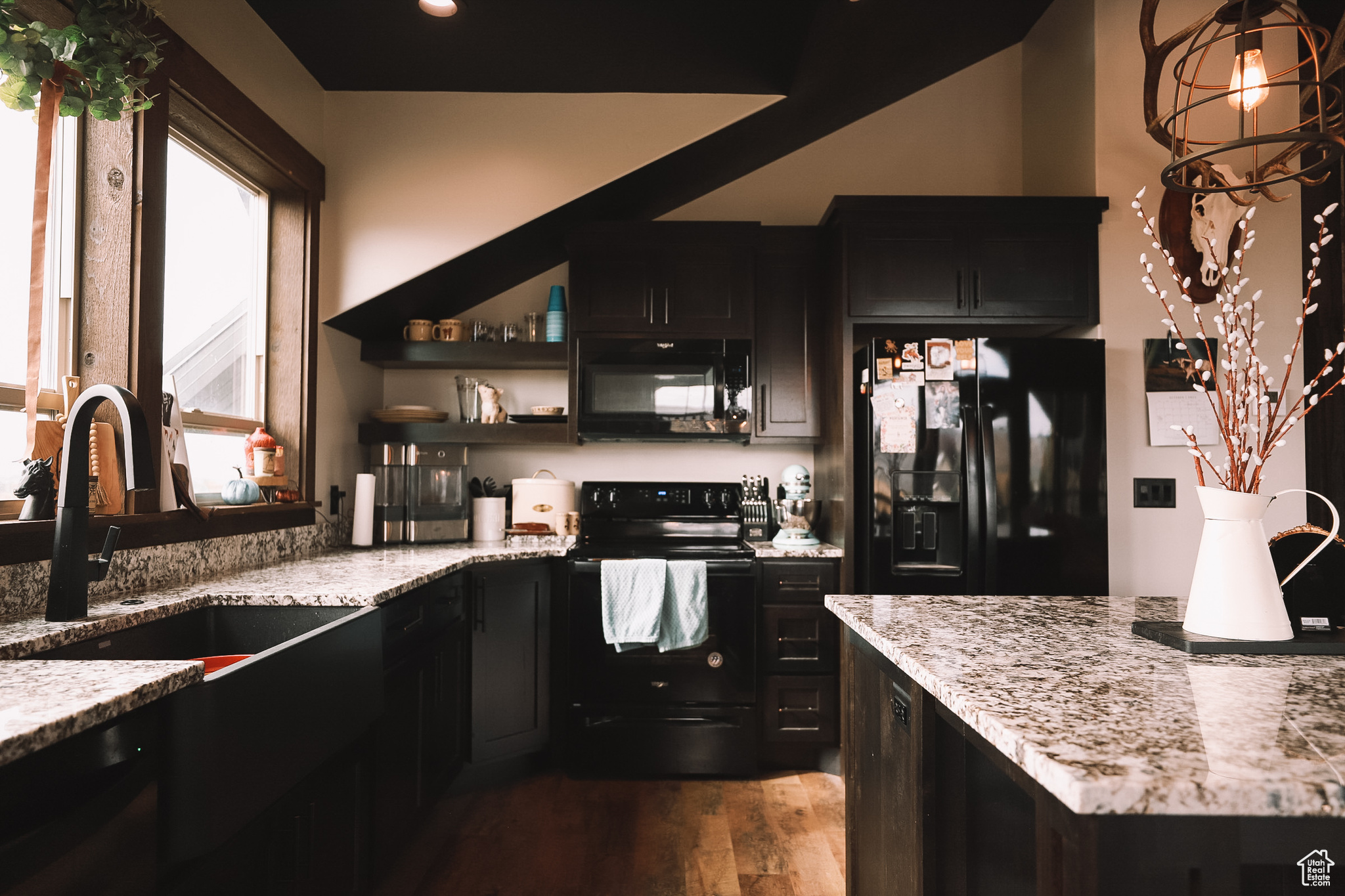 Kitchen featuring sink, dark hardwood / wood-style flooring, light stone counters, and black appliances