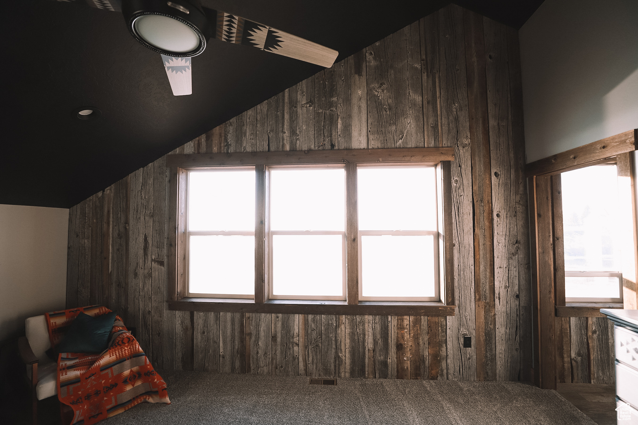 Primary bedroom with wood walls, carpet floors, and a healthy amount of sunlight