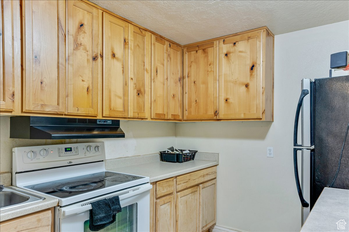 Kitchen with light brown cabinetry, electric range, a textured ceiling, and black fridge