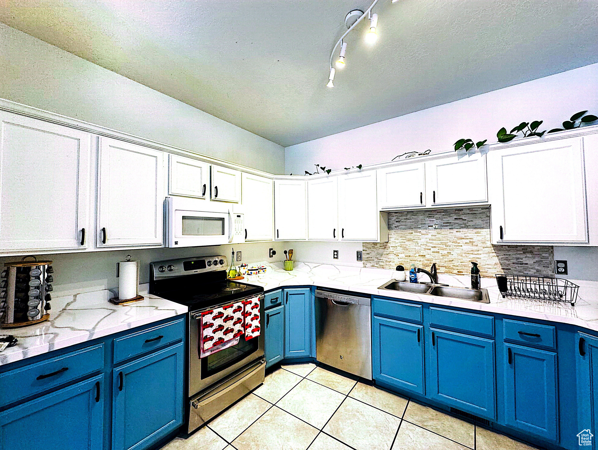 Kitchen featuring appliances with stainless steel finishes, rail lighting, light tile floors, sink, and blue cabinetry