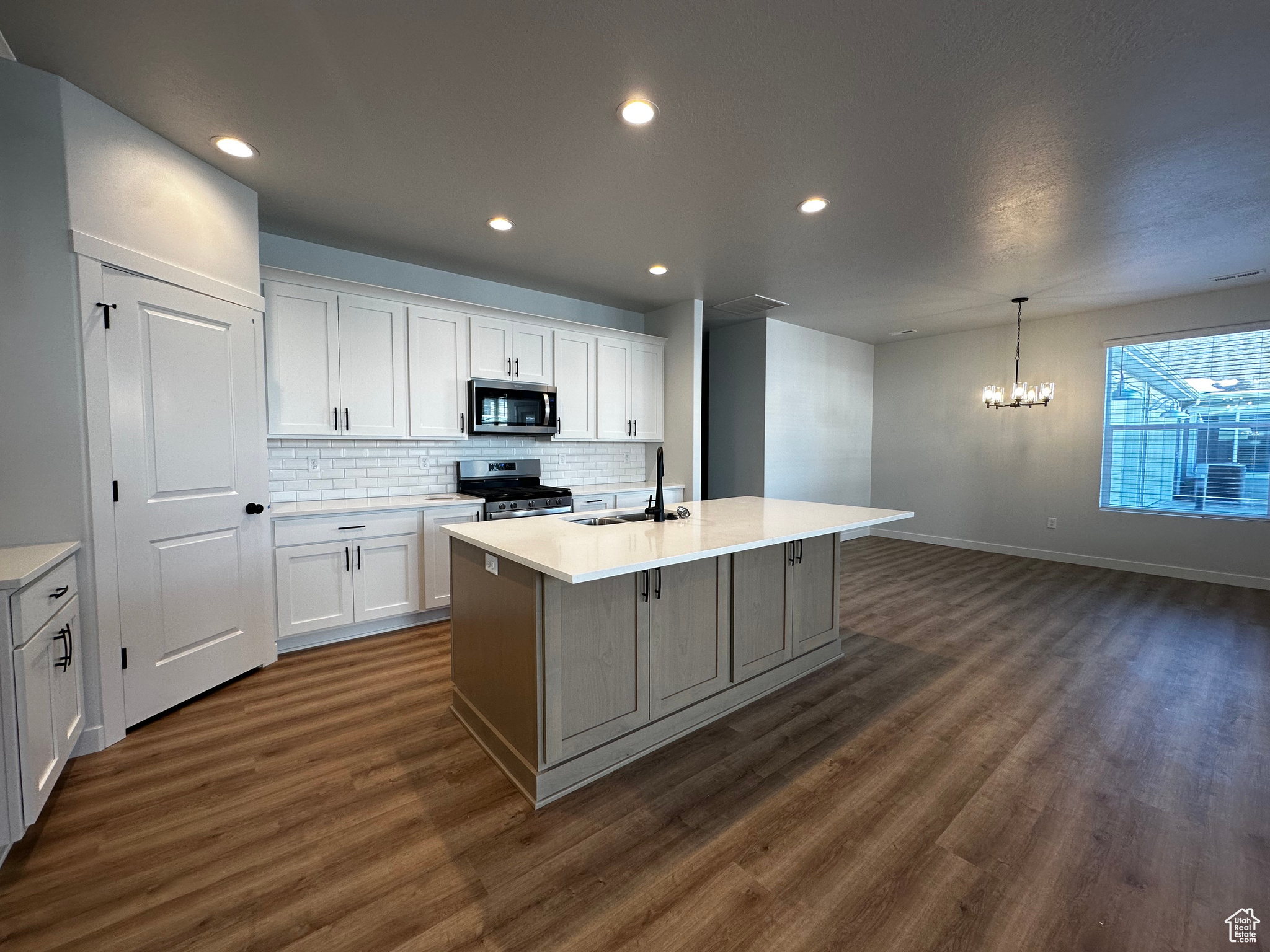 Kitchen with stainless steel appliances, white cabinets, an island with sink, and dark hardwood / wood-style flooring