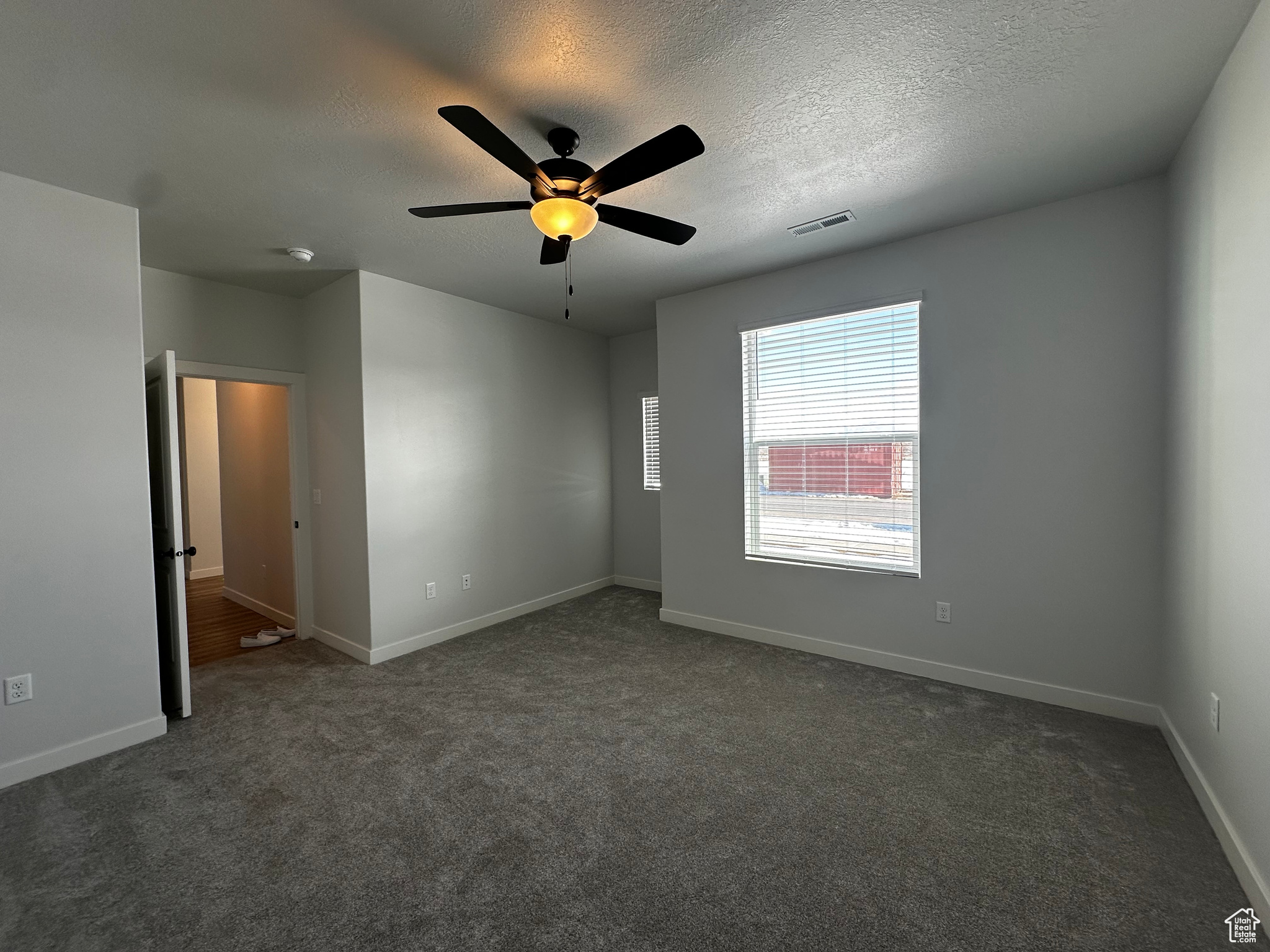 Carpeted spare room featuring a textured ceiling and ceiling fan