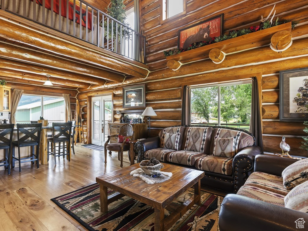 Living room with log walls, a towering ceiling, french doors, and light wood-type flooring