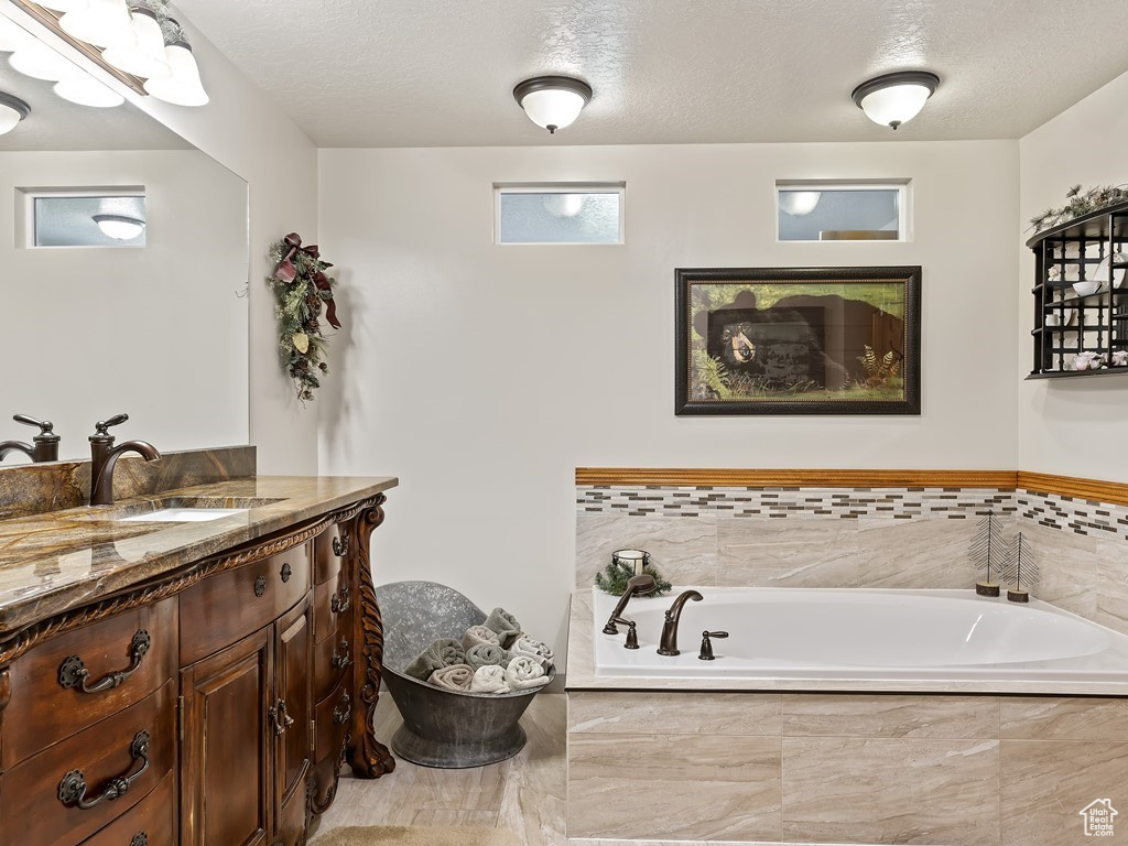 Bathroom featuring vanity, a textured ceiling, and tiled tub