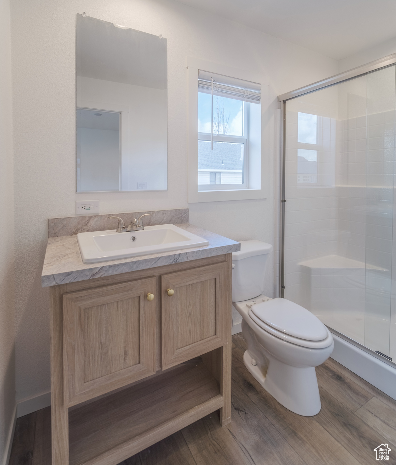 Bathroom featuring wood-type flooring, toilet, vanity, and a shower with door