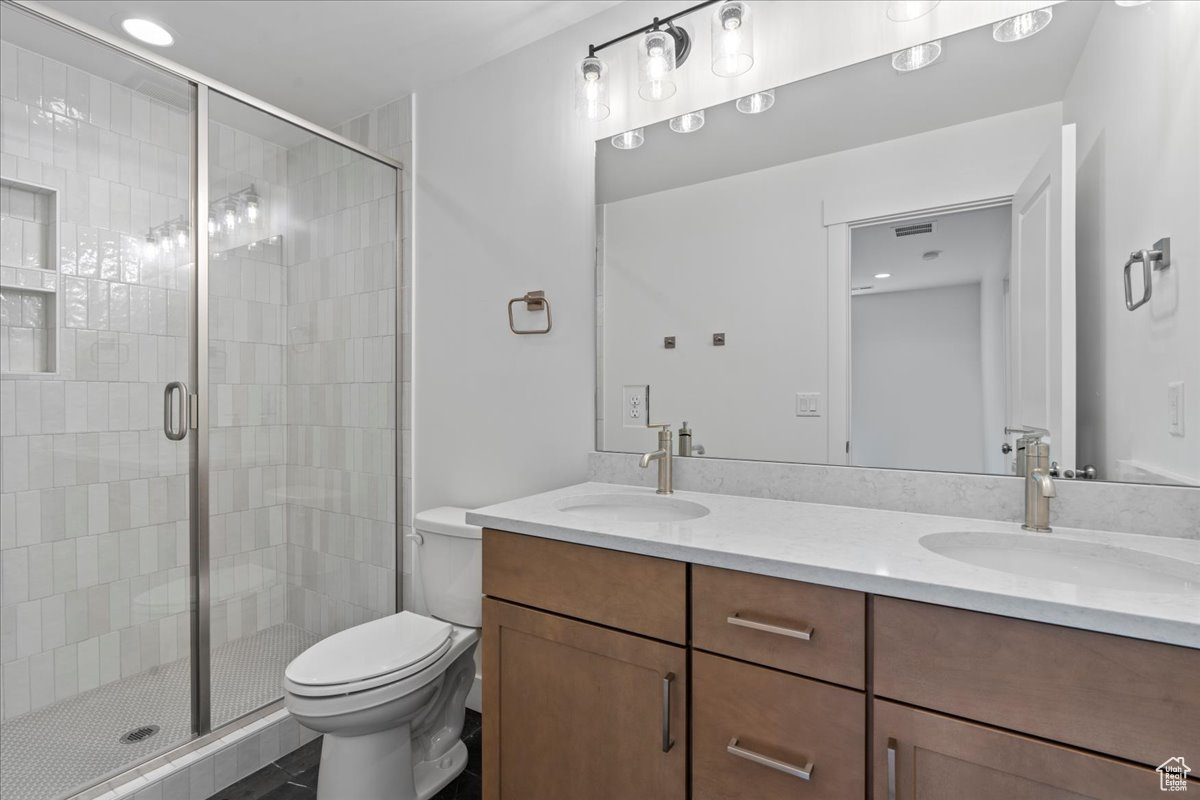 Bathroom with toilet, double sink vanity, and a shower with door