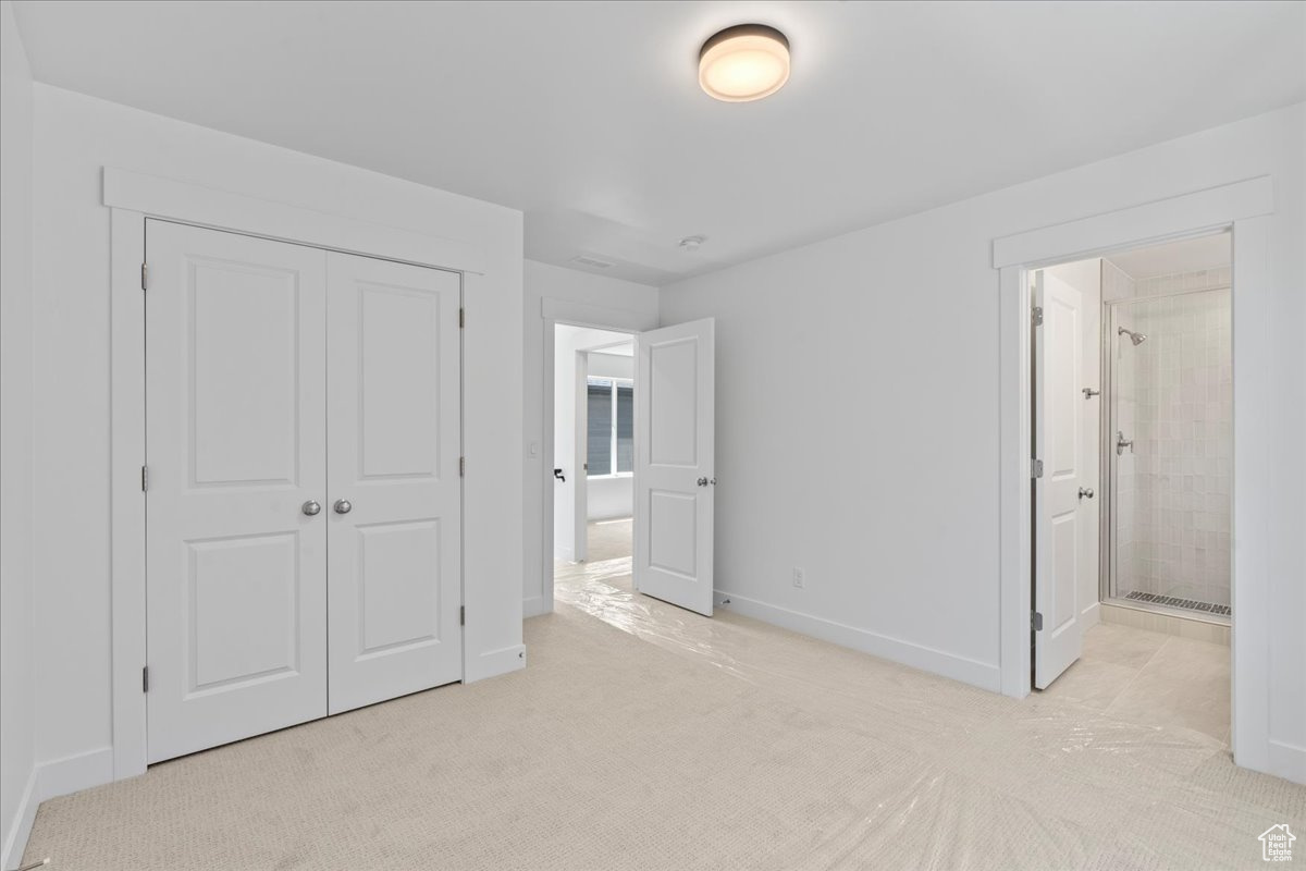 Unfurnished bedroom featuring ensuite bath, a closet, and light colored carpet