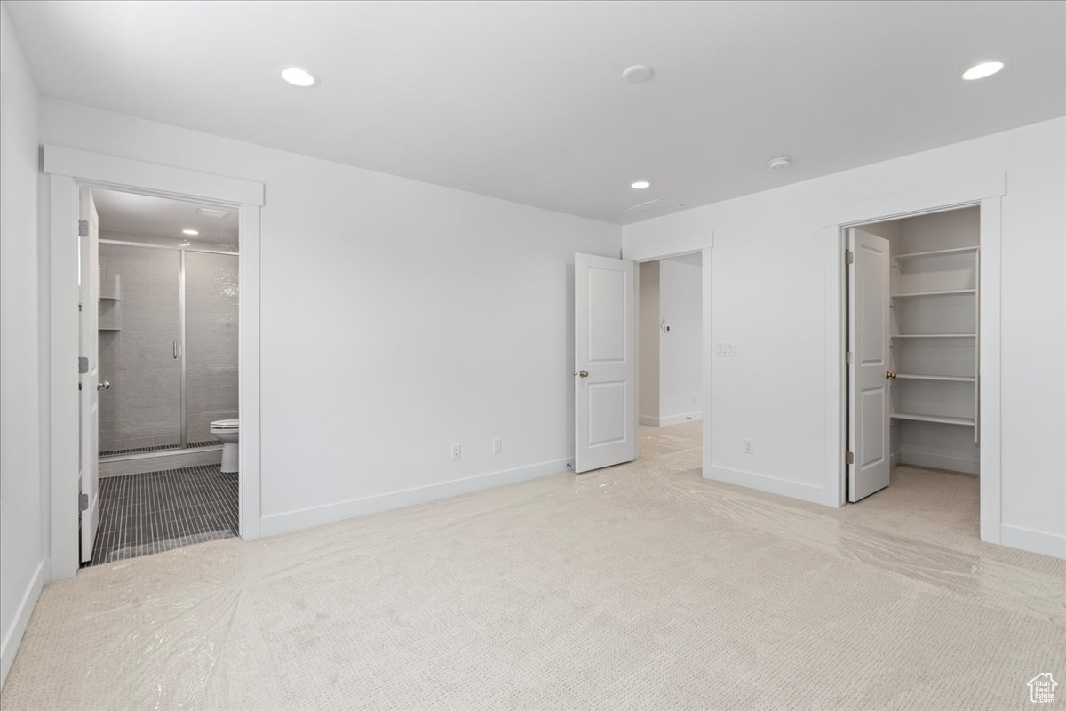 Unfurnished bedroom featuring a spacious closet, a closet, connected bathroom, and light colored carpet