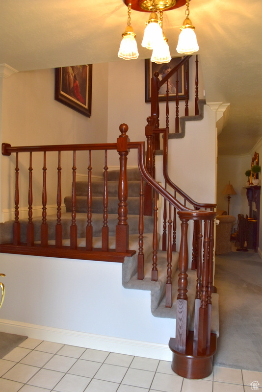 Staircase featuring crown molding, a chandelier, and light colored carpet
