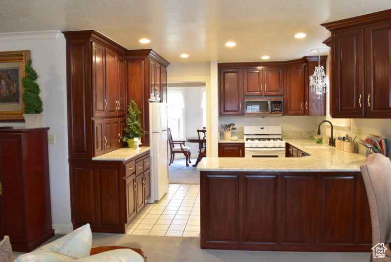 Kitchen with kitchen peninsula, light stone countertops, white appliances, pendant lighting, and sink