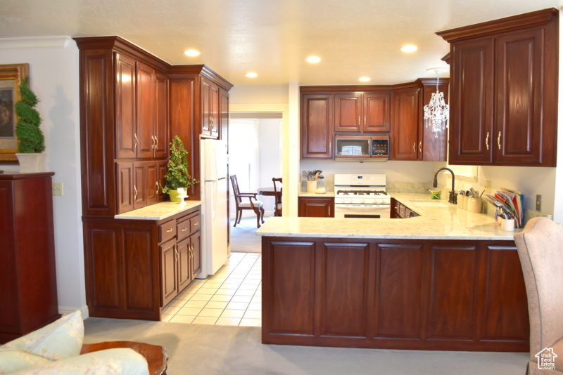 Kitchen featuring sink, light carpet, white appliances, and decorative light fixtures