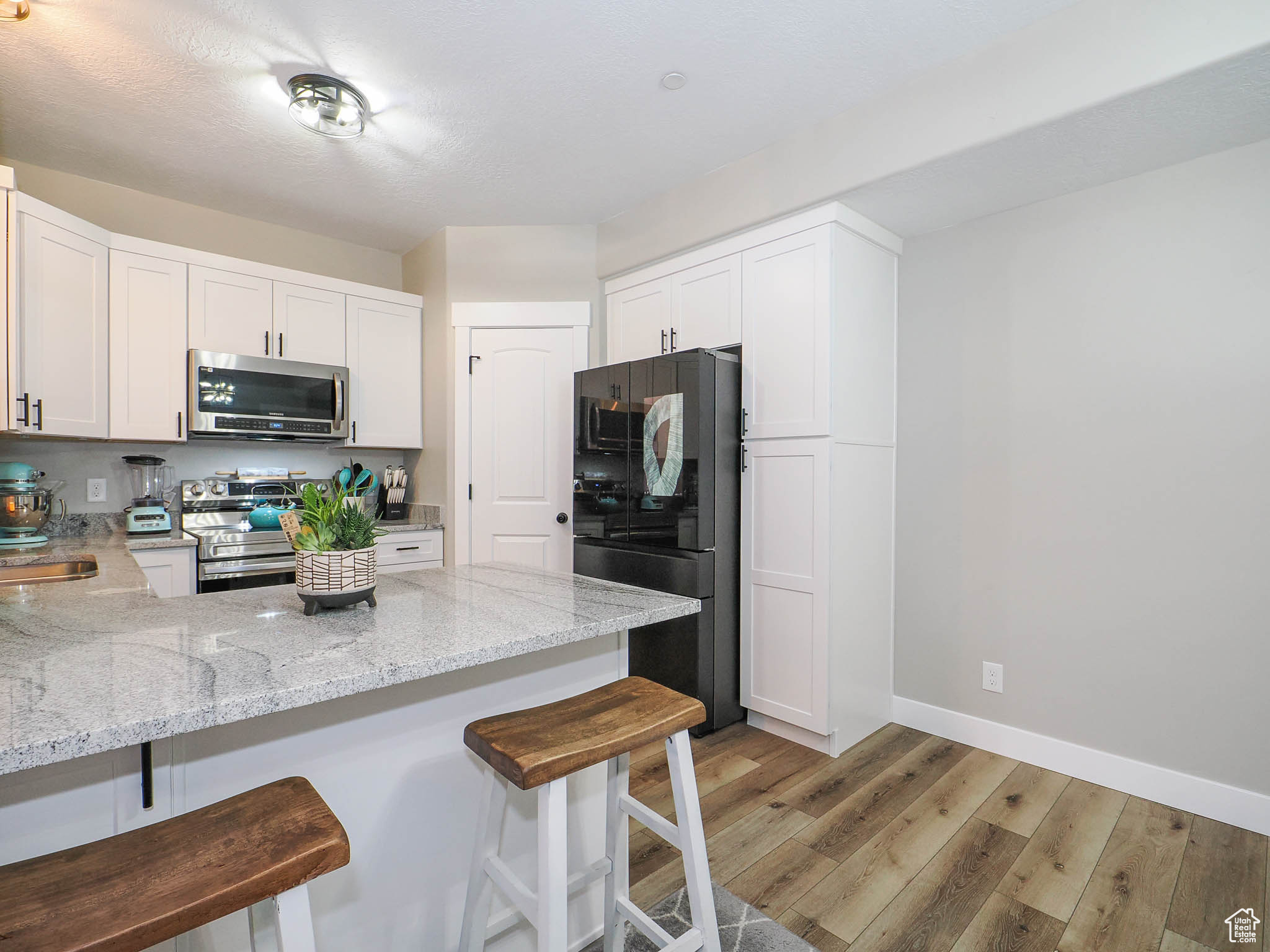Kitchen with a breakfast bar, white cabinets, light hardwood / wood-style floors, and stainless steel appliances