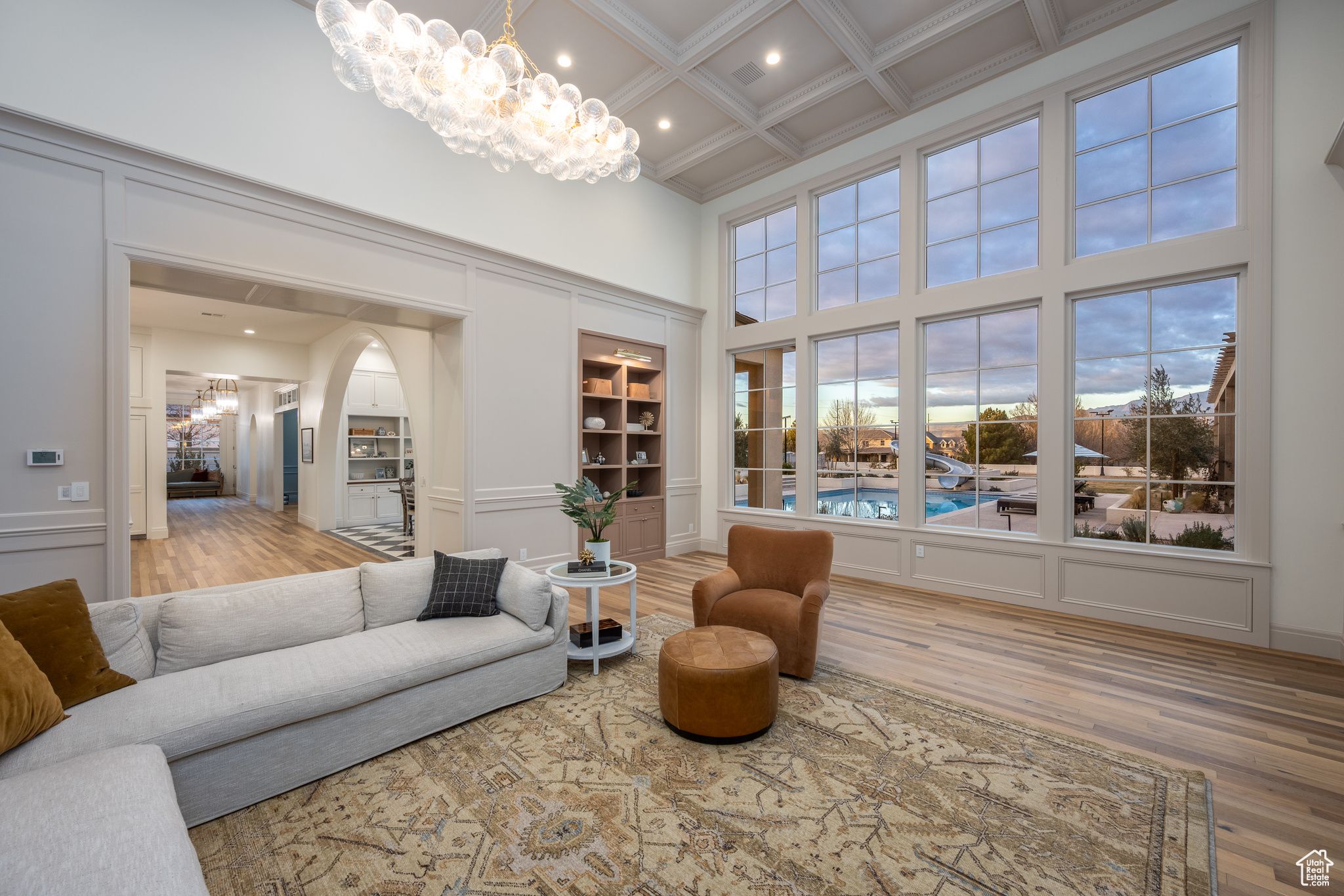 Living room with coffered ceiling, beamed ceiling, light hardwood / wood-style flooring, a high ceiling, and a notable chandelier