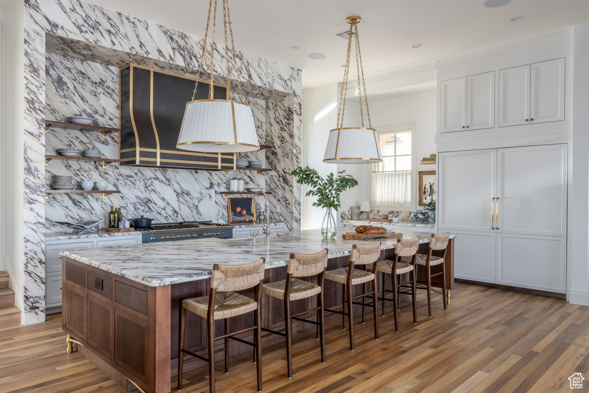 Kitchen with a kitchen breakfast bar, light stone countertops, hanging light fixtures, a center island with sink, and hardwood / wood-style flooring