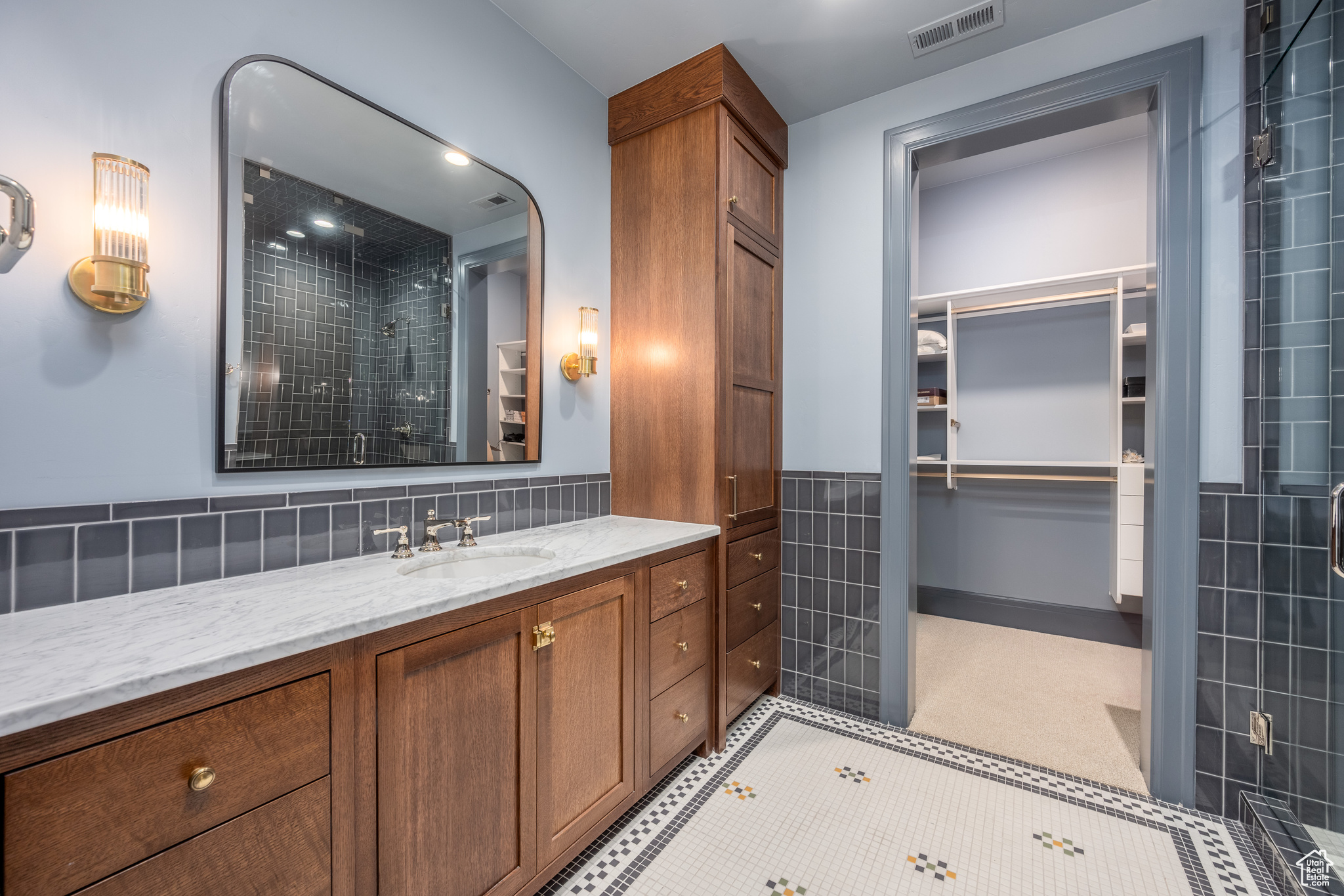 Bathroom with large vanity, tile walls, tile floors, backsplash, and a shower with door