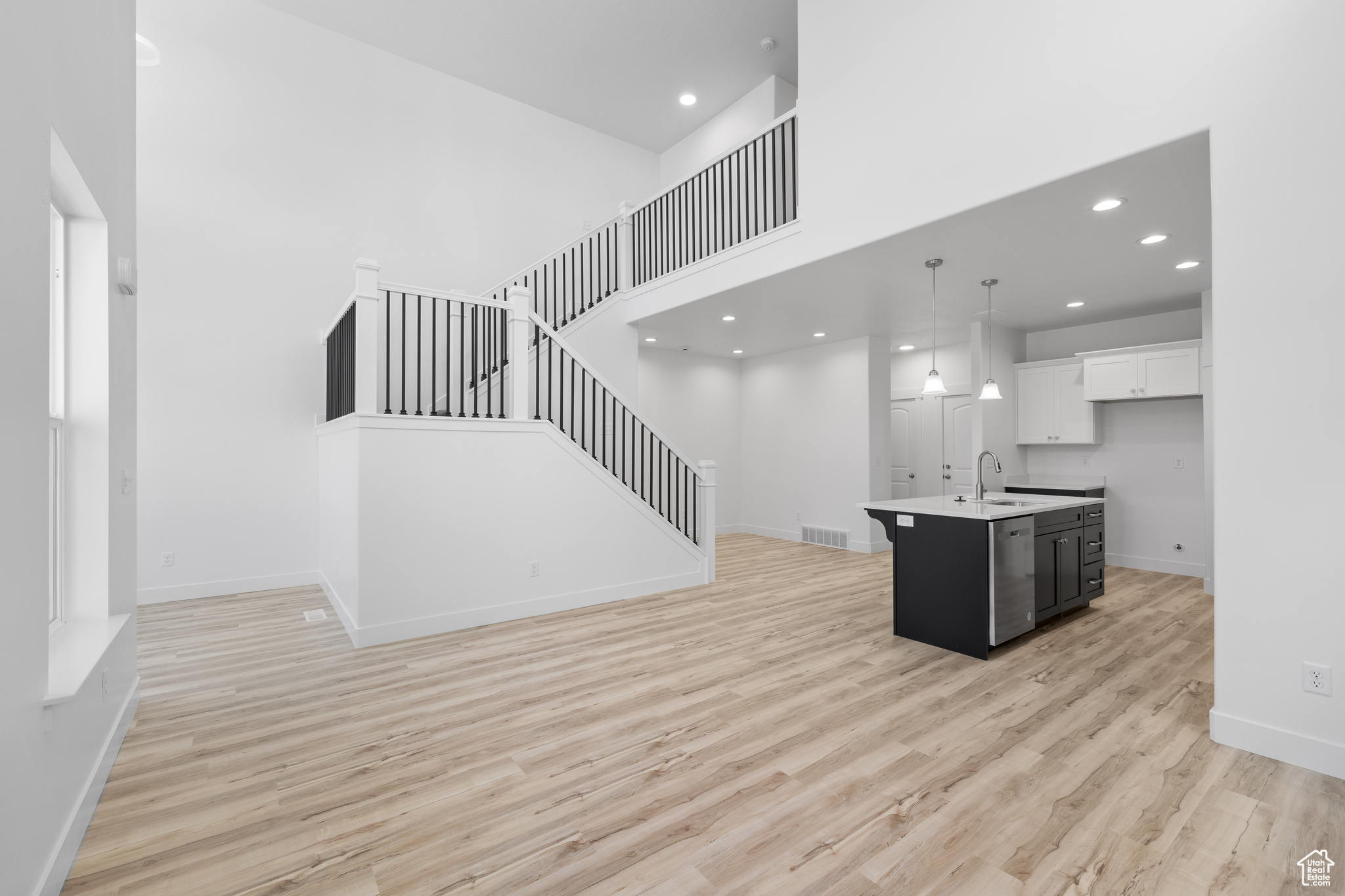 Interior space featuring an island with sink, decorative light fixtures, light wood-type flooring, a high ceiling, and sink