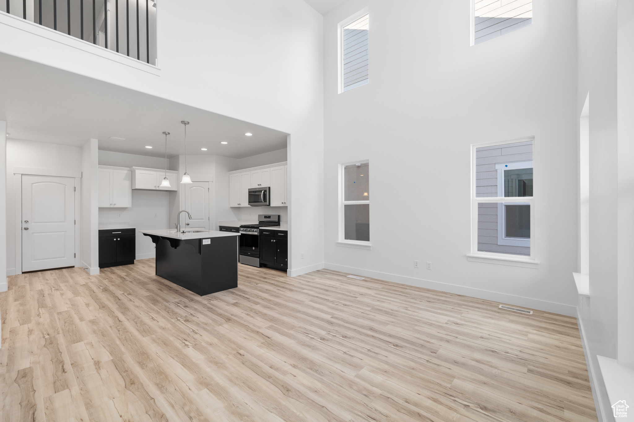 Kitchen featuring light hardwood / wood-style floors, stainless steel appliances, a kitchen island with sink, a high ceiling, and pendant lighting