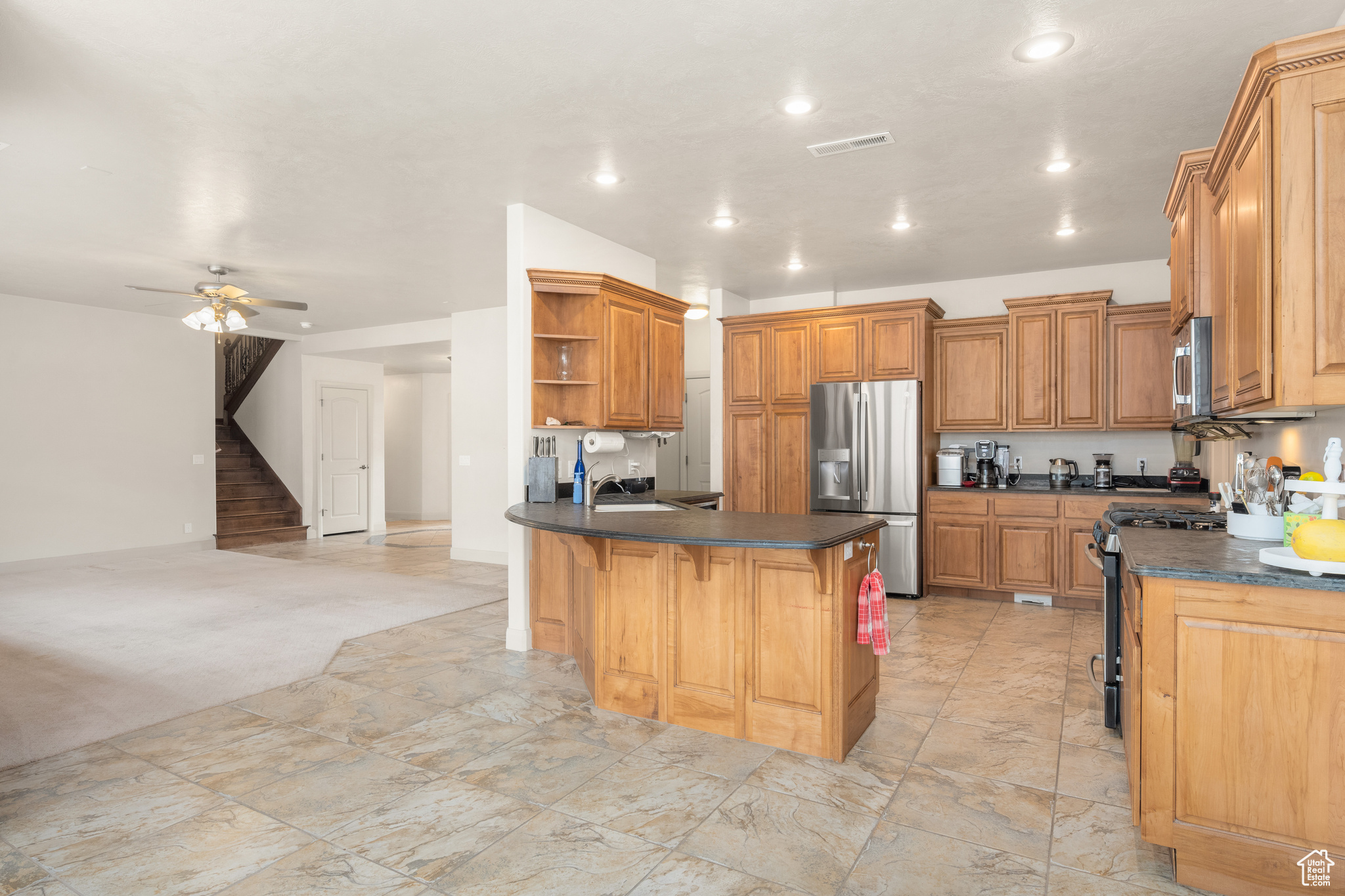 Kitchen featuring a kitchen breakfast bar, ceiling fan, light colored carpet, appliances with stainless steel finishes, and sink