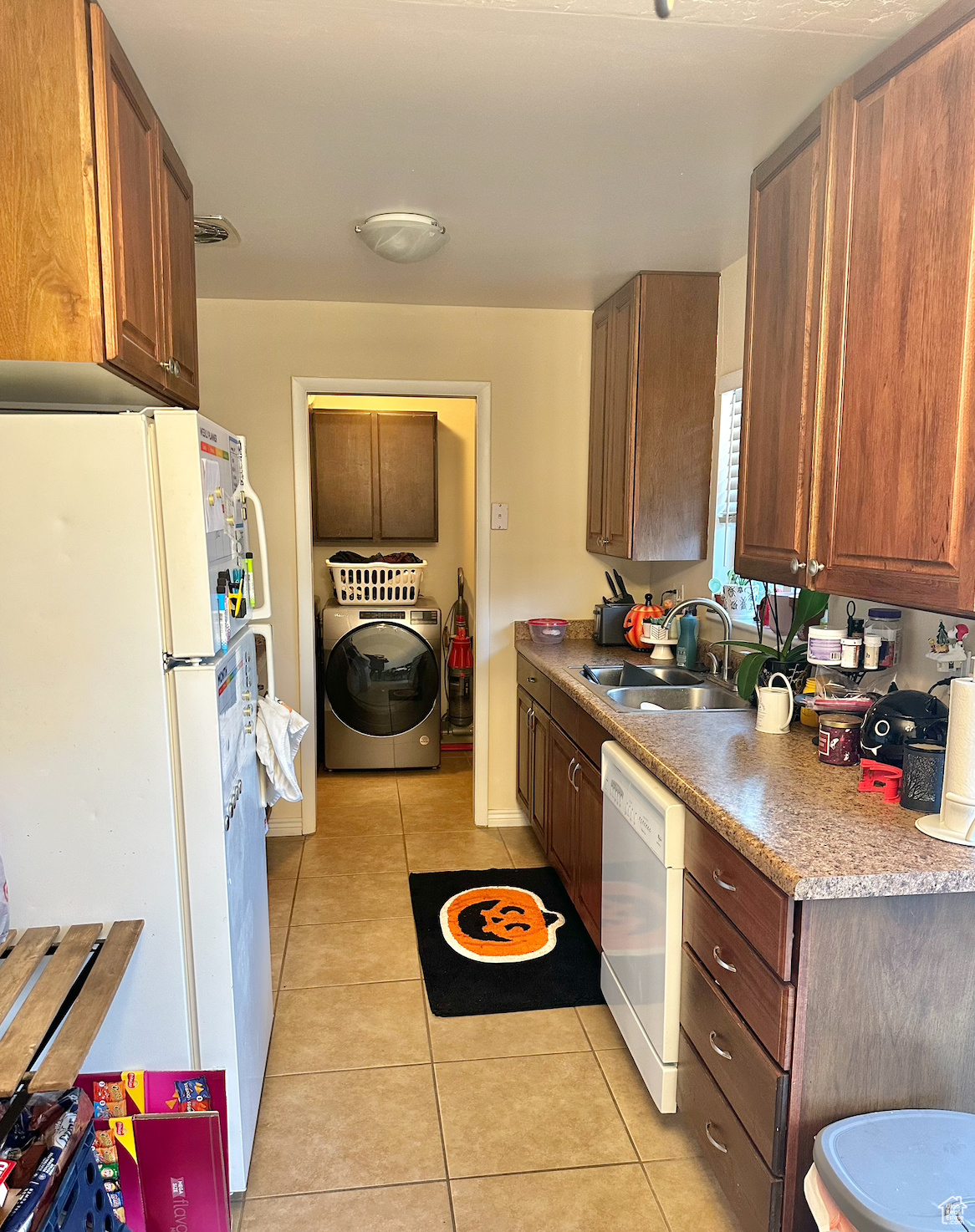 Kitchen featuring washer / dryer, white appliances, light tile floors, and sink