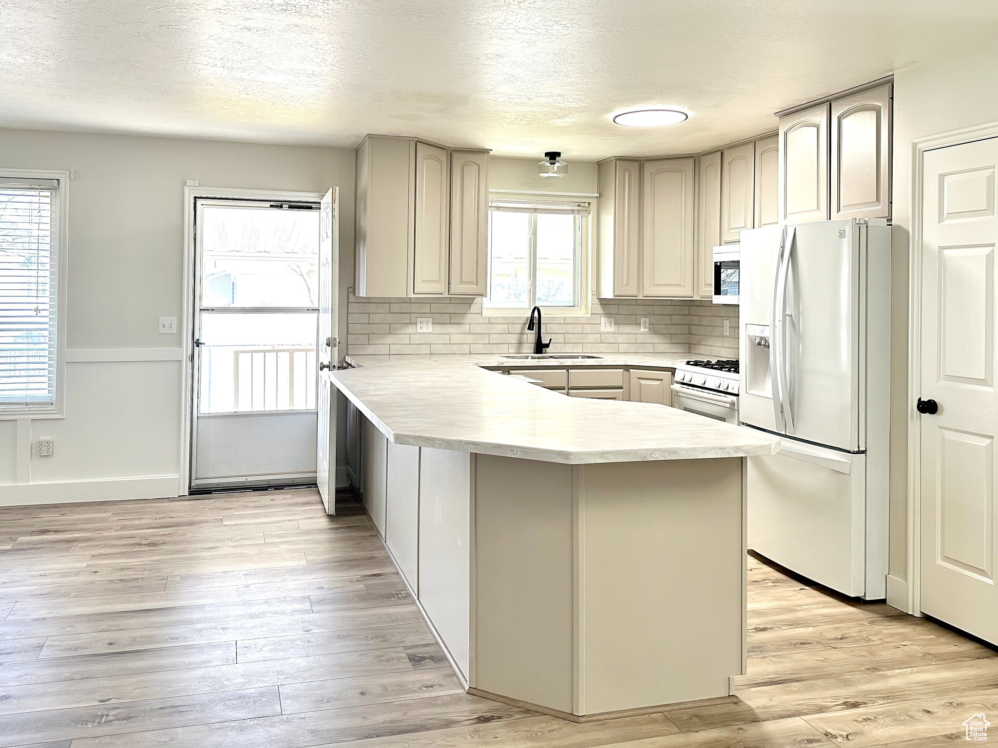 Kitchen featuring kitchen peninsula, white appliances, light hardwood / wood-style flooring, backsplash, and sink
