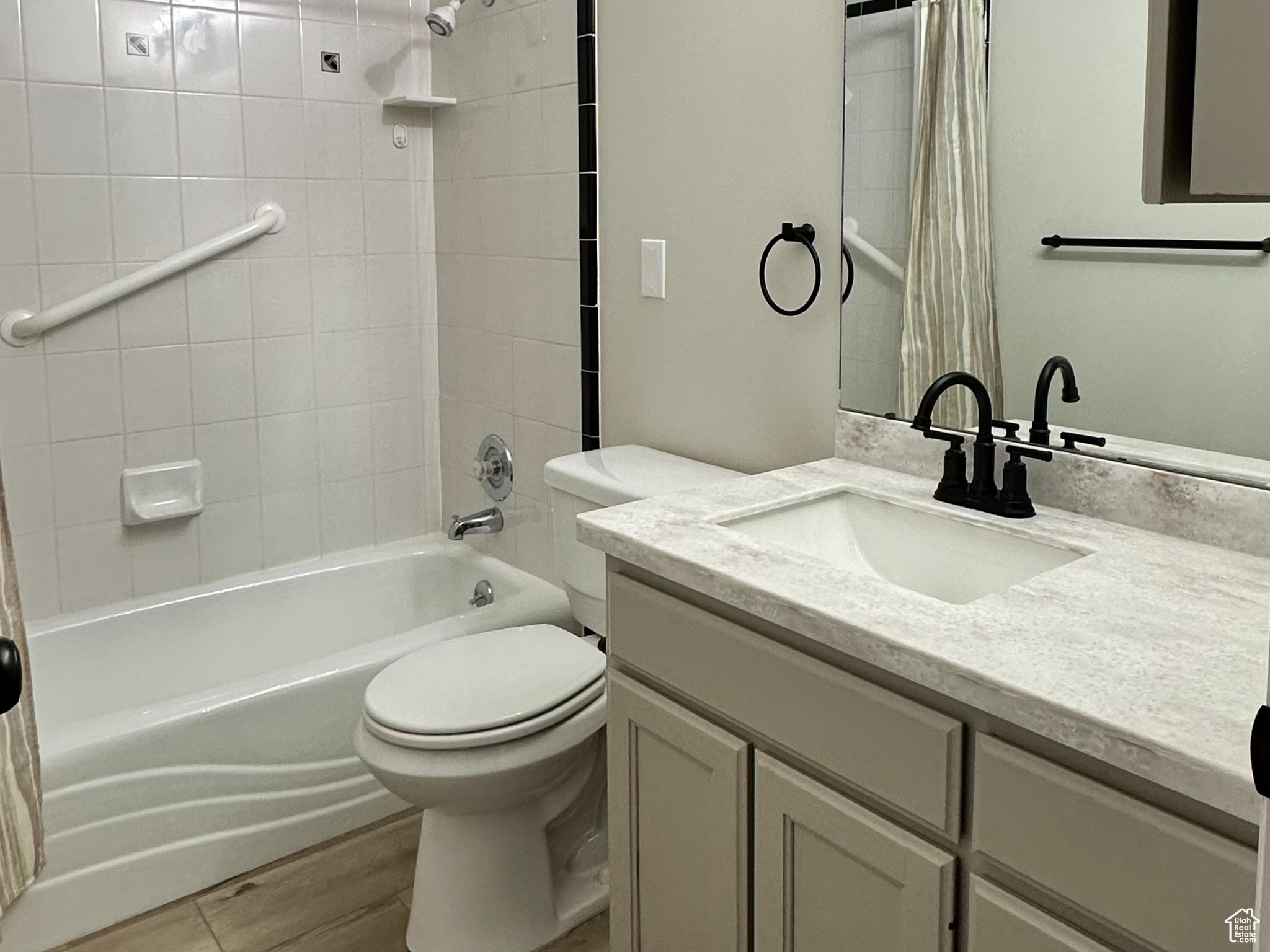Full bathroom with oversized vanity, toilet, shower / bathtub combination with curtain, and hardwood / wood-style flooring