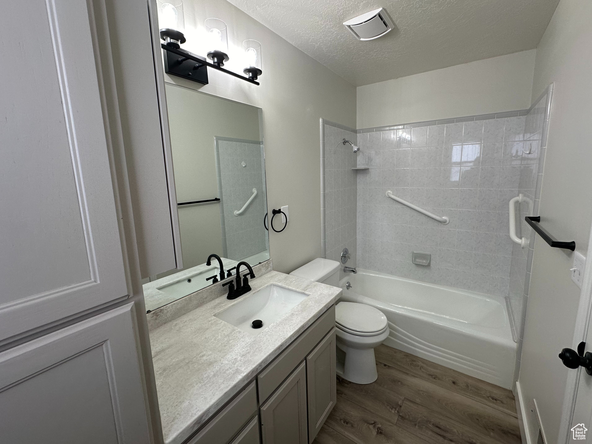 Full bathroom with toilet, large vanity, wood-type flooring, tiled shower / bath, and a textured ceiling