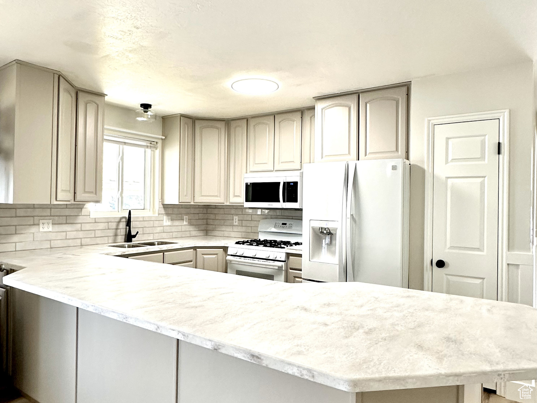 Kitchen featuring light hardwood / wood-style floors, light stone countertops, white appliances, kitchen peninsula, and sink